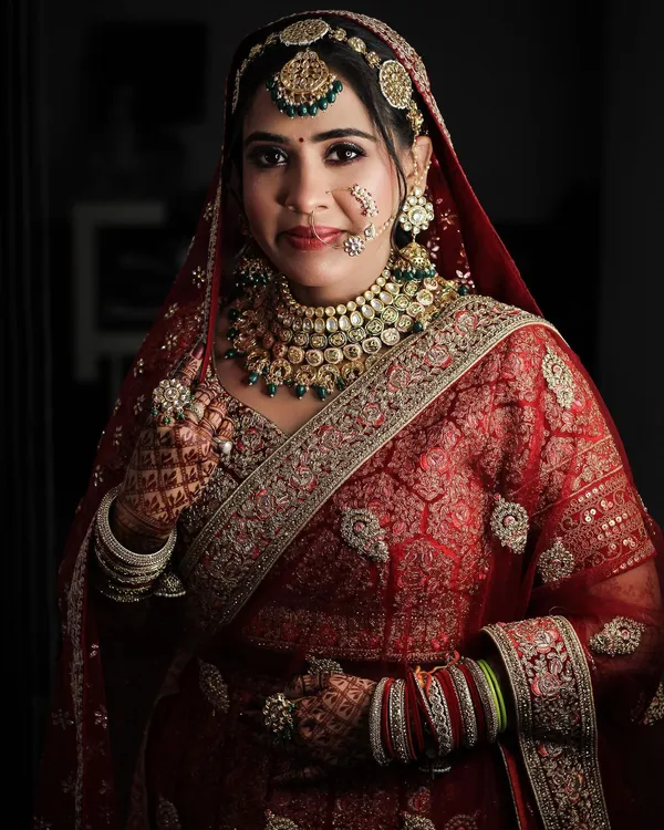 Bride in a maroon Banarasi lehenga with a gold border and layered necklaces