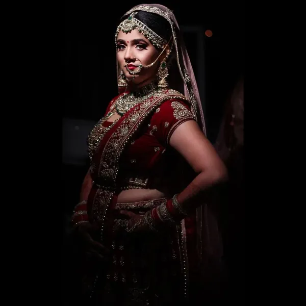 Full-length bride in a maroon lehenga against a dark backdrop