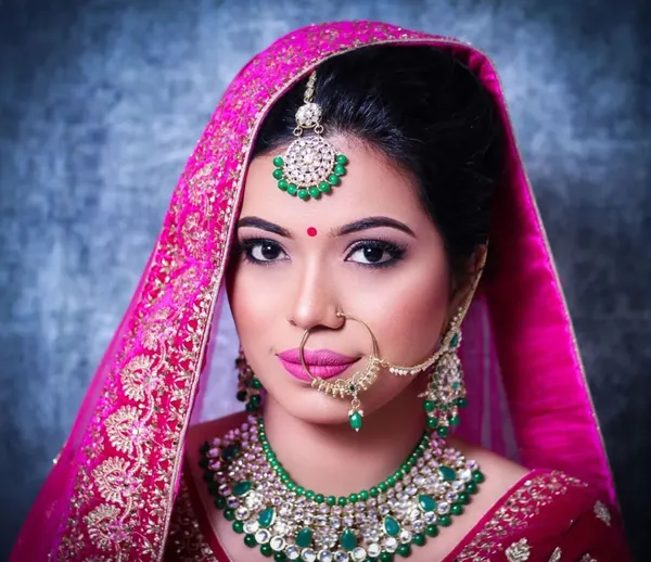 Bride in a pink dupatta with emerald and kundan jewellery