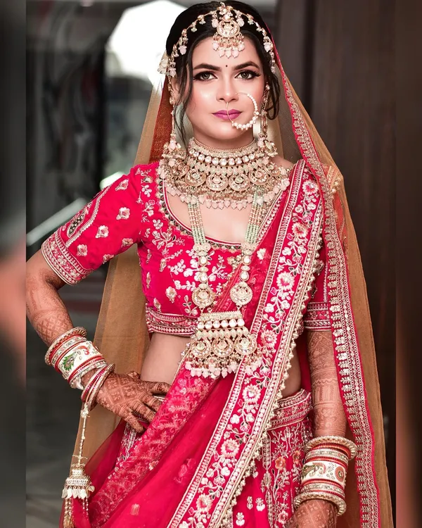 Full-length bridal portrait in a pink and red lehenga with gold jewellery