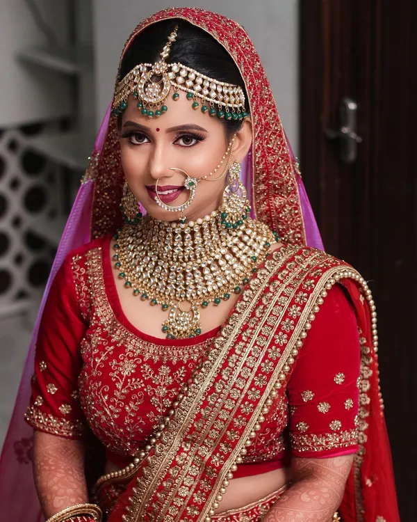 Bride in red with a heavy gold and kundan bridal necklace, eyes lowered