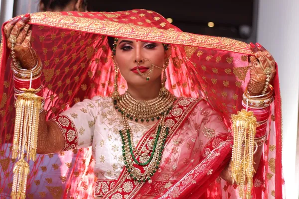 Close detail of a bridal nath and lip colour under a red veil